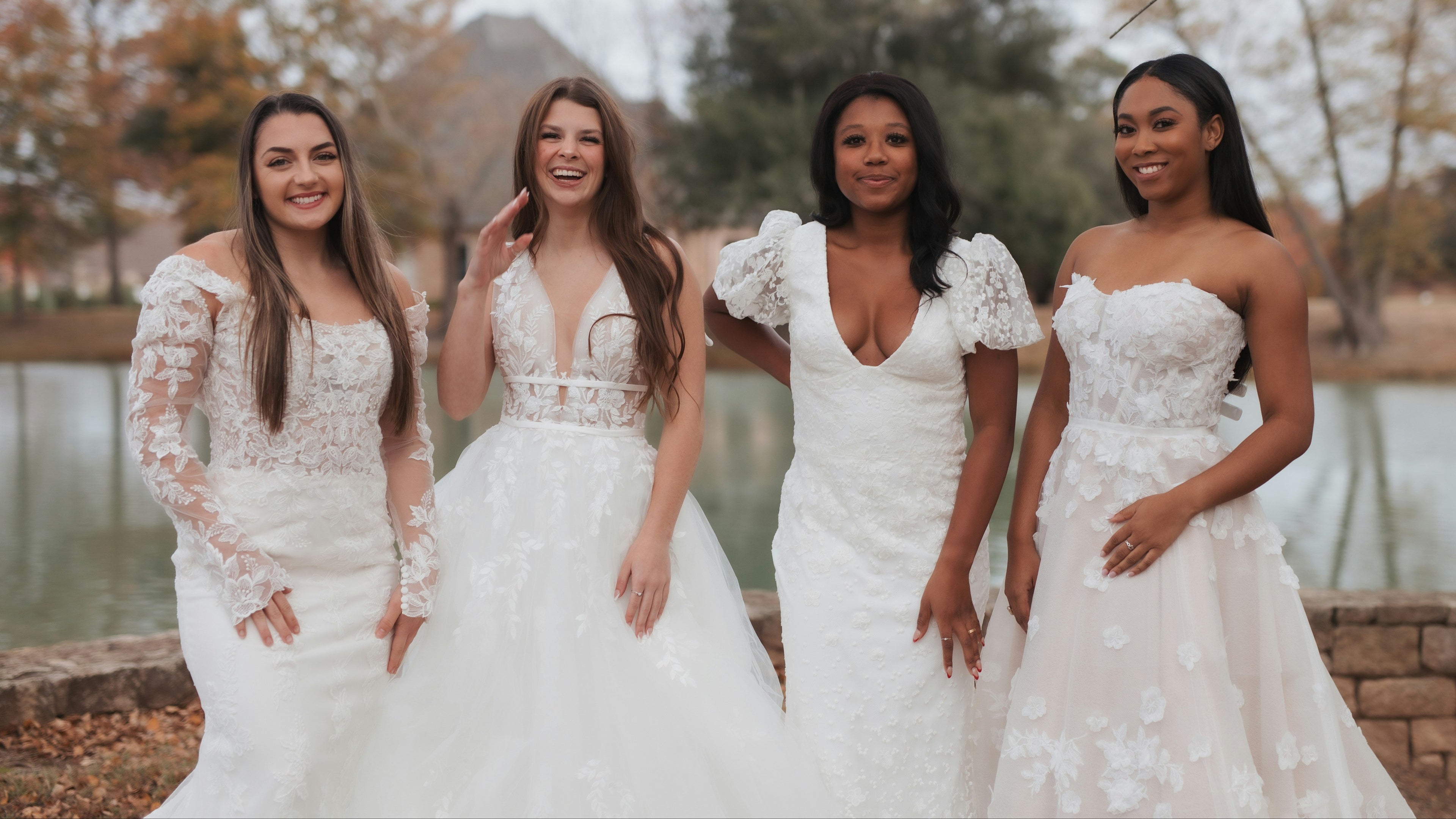 Four women in wedding dresses standing by a lake.